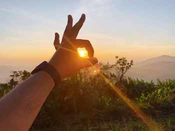 Hand holding sun against sky during sunset