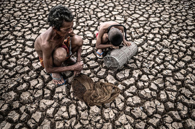 High angle view of senior man with grandson crouching on arid land