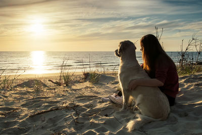 Woman sitting with dog at beach during sunset
