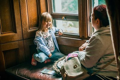 Rear view of girl sitting on window at home