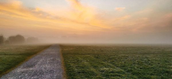 Road amidst field against sky during foggy weather