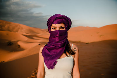 Portrait of young woman standing in desert against sky