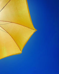 Low angle view of yellow umbrella against clear blue sky