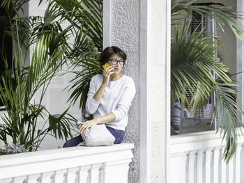 Young woman using mobile phone while standing against building