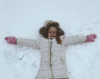 High angle view of young woman with arms outstretched lying in snow