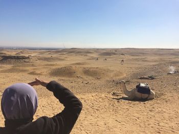 Woman looking at camel on desert against clear sky