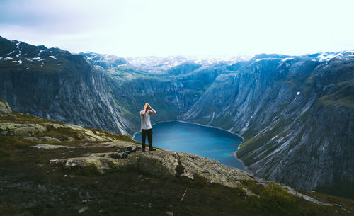 Man standing on rock by lake against sky