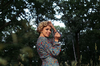 Portrait of woman with hand in hair while standing against trees