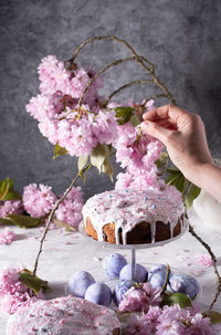 A woman decorates a homemade easter cake with pink sakura flowers,spring blossom