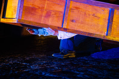 Low section of man holding cabinet on road at night