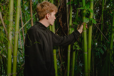 Side view of woman standing amidst plants in forest