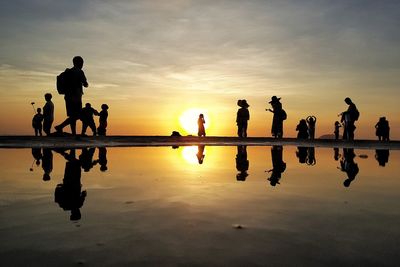 Silhouette people at beach against sky during sunset