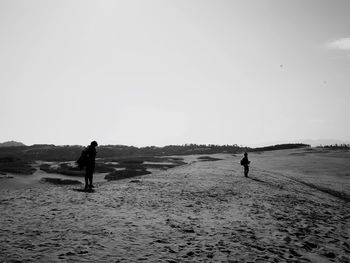 Silhouette people standing on beach against clear sky