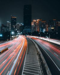 Light trails on road by illuminated buildings in city at night