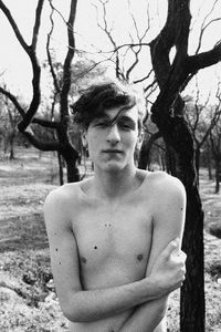 Portrait of young man standing by tree trunk