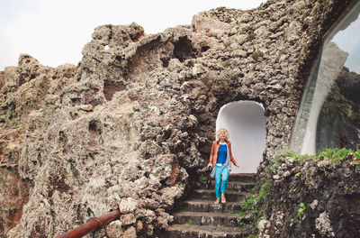 Woman climbing down steps on cliff against mountain