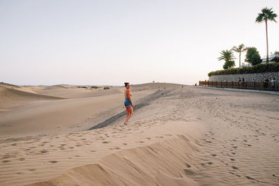 Rear view of woman walking at beach against clear sky