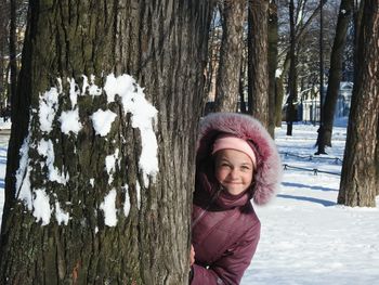Portrait of smiling young woman standing on tree trunk during winter