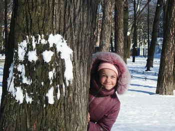 Portrait of smiling girl standing by tree trunk during winter