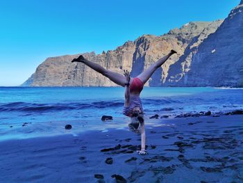 Rear view of woman jumping in sea against clear sky