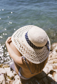Woman with hat sitting on the beach by the sea