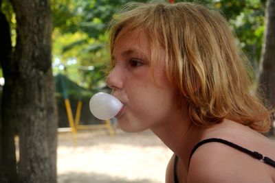 Close-up of girl blowing chewing gum by trees