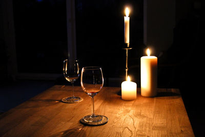 Illuminated candles by wineglass on table in darkroom