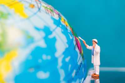 Close-up of figurine by globe against blue background
