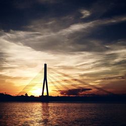 Silhouette bridge over sea against sky during sunset