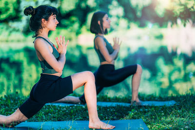 Young women meditating, practicing yoga by the water