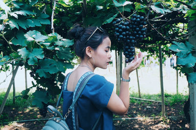 Side view of young woman standing against plants