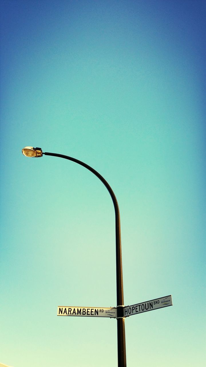 clear sky, low angle view, communication, copy space, blue, text, western script, guidance, street light, lighting equipment, information, pole, sign, road sign, no people, metal, arrow symbol, outdoors, day, directional sign