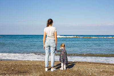 Rear view of woman standing on beach against sea