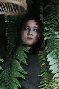 Thoughtful young woman looking away while standing by plants