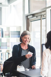 Businesswoman reading card while standing at counter in office