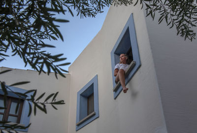 Low angle view of girl in window against sky