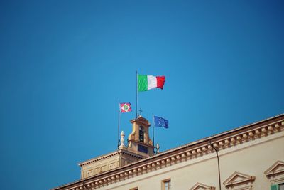 Low angle view of flags waving against clear blue sky