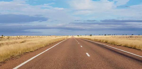 Road passing through field against sky