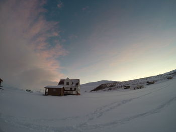 Built structure on snow covered landscape against sky during sunset