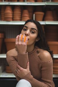 Portrait of teenage girl eating orange against flower pots on shelves in store