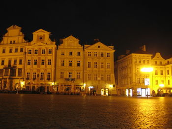 Illuminated buildings by street against sky at night