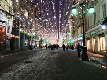 People on illuminated street amidst buildings in city at night