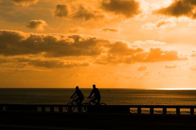 Silhouette people riding on sea against sky during sunset