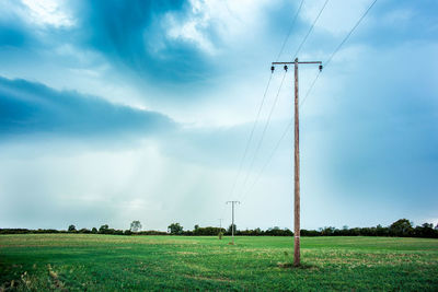 Electricity pylon on grassy field against cloudy sky