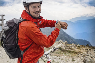 Portrait of mountain biker showing smart watch while standing on cliff