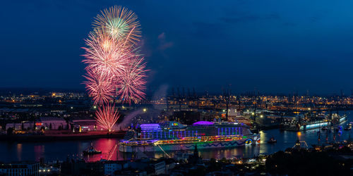 Firework display over illuminated city against sky at night