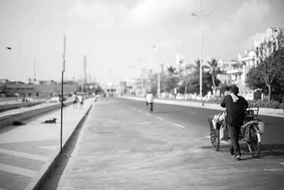 Rear view of street vendor walking on road with tricycle