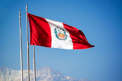 Low angle view of peruvian flag waving against clear blue sky