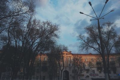 Low angle view of bare trees against cloudy sky