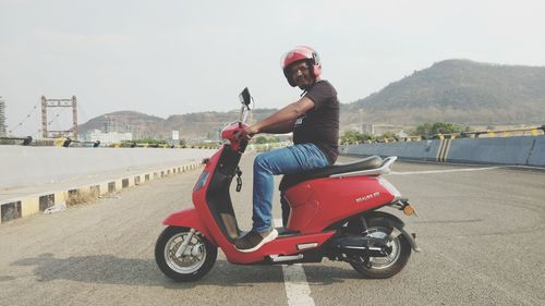 Portrait of man riding motorcycle on road against sky